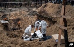 Criminaliștii inspectează un cadavru găsit în groapa comună de lângă Izium, 16 septembrie 2022