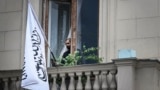An official uses his smartphone next to the flag of the Islamic Emirate of Afghanistan at the balcony of the Afghan Embassy in Moscow on July 4.