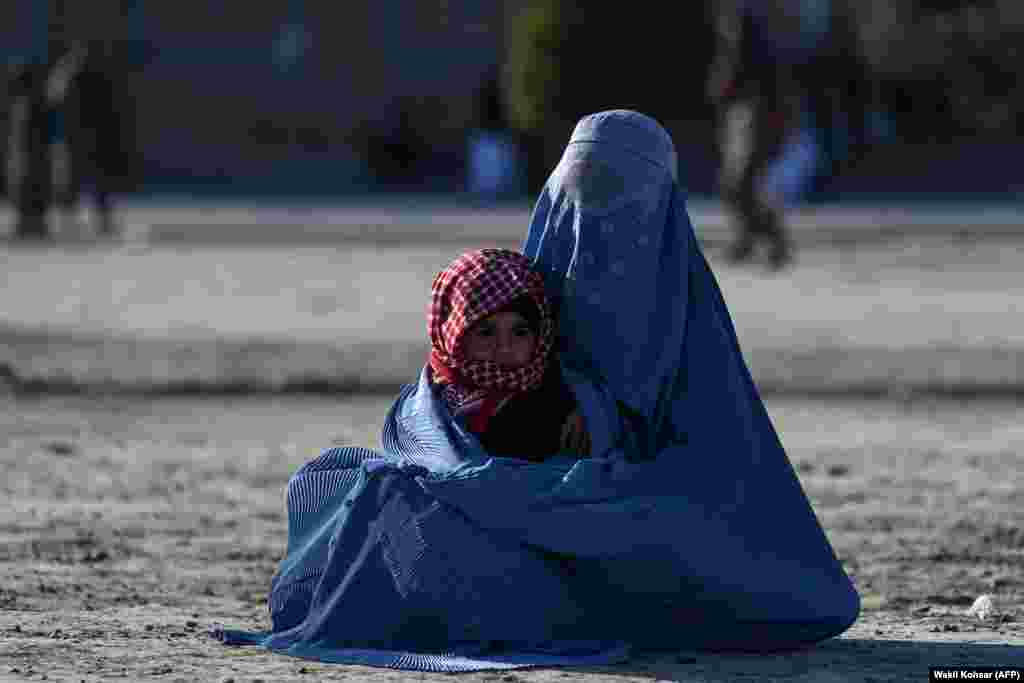 An Afghan burqa-clad woman holds a child as she begs for alms in front of the Great Mosque of Herat.&nbsp;