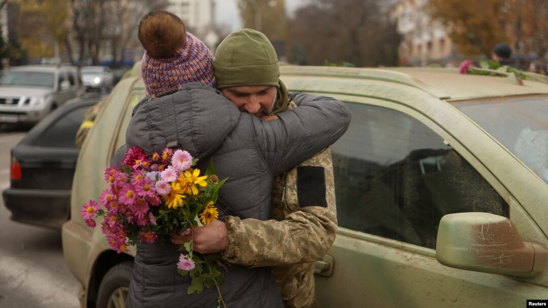 O femeie și un soldat ucrainean cu flori în mână sunt surprinși în timp ce se îmbrățișează în centrul orașului Herson, eliberat săptămâna trecută de forțele ucrainene după retragerea Rusiei, 13 noiembrie 2022.