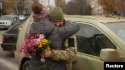 O femeie și un soldat ucrainean cu flori în mână sunt surprinși în timp ce se îmbrățișează în centrul orașului Herson, eliberat săptămâna trecută de forțele ucrainene după retragerea Rusiei, 13 noiembrie 2022.