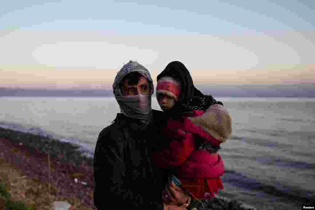 Një burrë mban fëmijën e tij gjatë ecjes në bregdetin grek, pas arritjes nga Turqia.&nbsp;