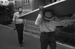 Un băbat cu o mască de protecție privește un bărbat care cară o ușă, în iulie 1988.