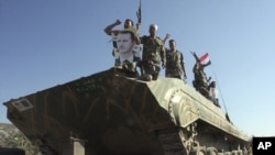 Syrian soldiers shout pro-President Bashar al-Assad slogans as they stand on their tank on a flatbed truck heading out of the city of Edleb on August 10.