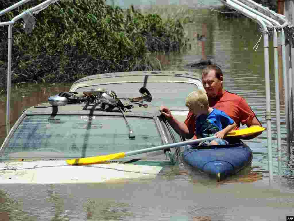 AUSTRALIA, Bundaberg : Scott Wogandt and his son Mitchell kayak past flooded cars in Bundaberg on December 31, 2010. Floods triggered by tropical cyclone Tasha have left entire towns under water and cut off many more over an area the size of France and Germany combined. AFP PHOTO / Torsten BLACKWOOD 