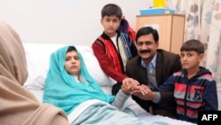 Malala Yousafzai, who was shot in the head by Taliban gunmen for campaigning for the right to an education, sitting on her bed amid her mother Toorpekai Yousufzai (L), brothers Khushal Khan (3rd R) and Apal Khan (R) and father