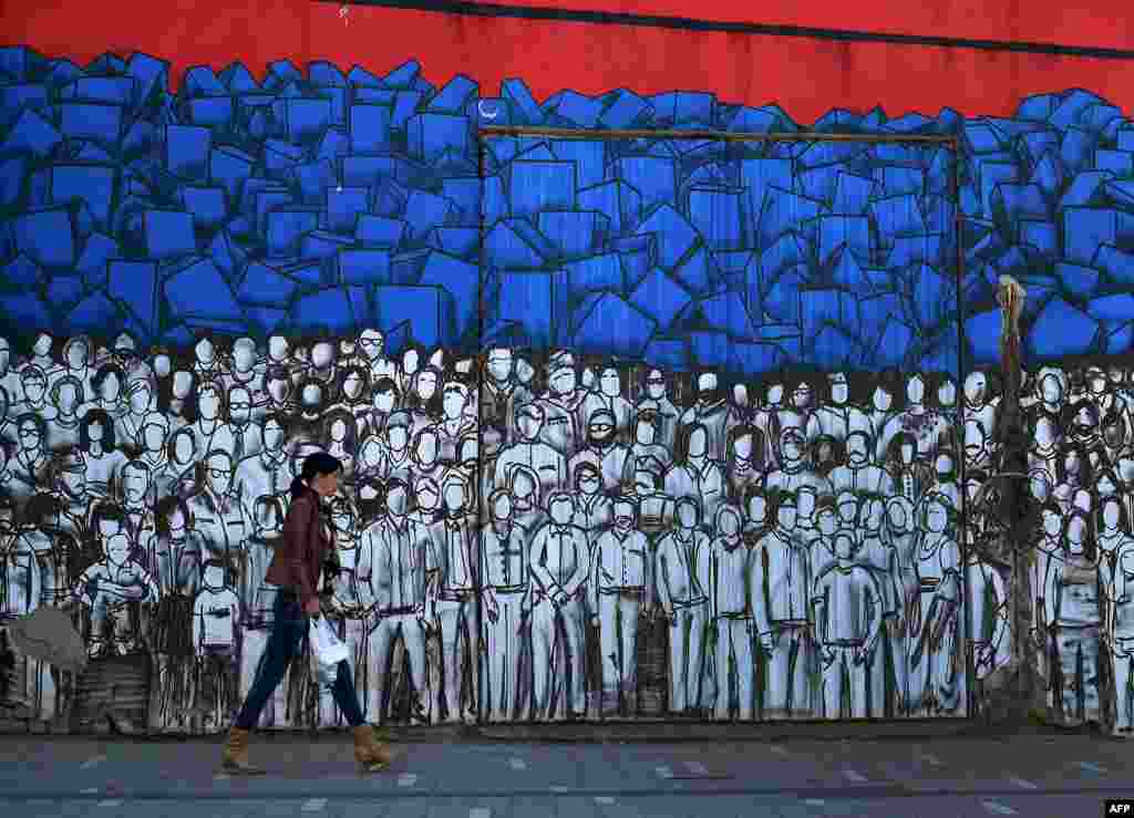A woman walks past a mural depicting many famous Serbs and the Serbian national flag in Belgrade. (AFP/Andrej Isakovic)