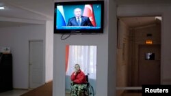 Мужчина в инвалидной коляске смотрит телевизор, где показывают выступление президента России Владимира Путина.