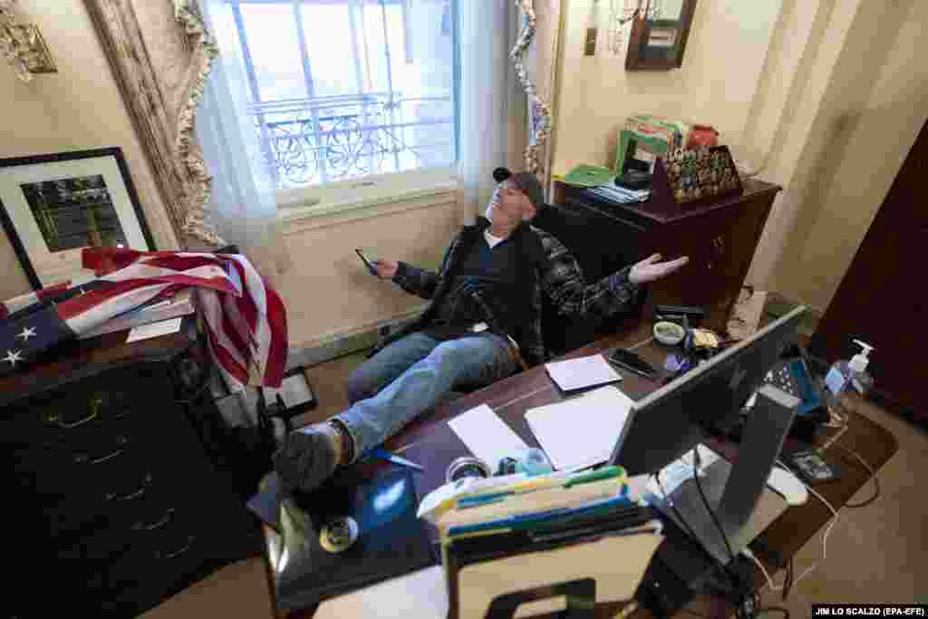 A supporter of U.S. President Donald J. Trump sits on the desk of U.S. House Speaker Nancy Pelosi, after supporters of US President Donald J. Trump breached the US Capitol security in Washington, DC, January 6, 2021. (EPA-EFE/JIM LO SCALZO)