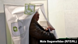 ამომრჩეველი საარჩევნო კაბინიდან გამოდის კონვერტით ხელში, რომელსაც ელექტრონულ მოწყობილობაში მოათავსებს