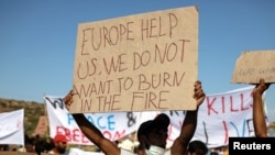 Един от протестиращите мигранти държи плакат, на който пише "Европа, помогни ни, не искаме да изгорим в пожара". 