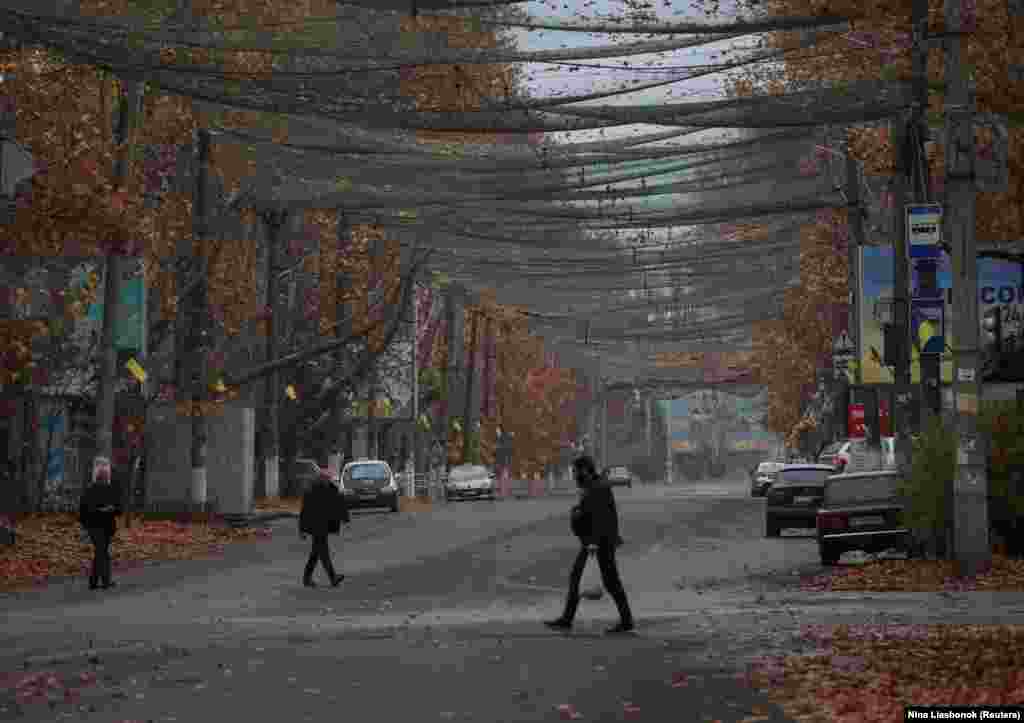 Disa qytetarë kalojnë në një rrugë të mbuluar me një rrjetë antidronë në qytetin e Hersonit më 11 nëntor 2025.