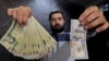 A money changer poses for the camera with a U.S dollar (R) and the amount being given when converting it into Iranian rials (L), at a currency exchange shop at Tehran's business district. File photo