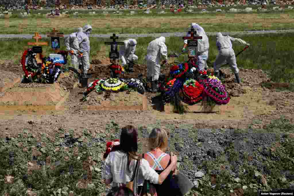 Mourners watch gravediggers burying a person who presumably died of COVID-19 in the special-purpose section of a graveyard on the outskirts of St. Petersburg, Russia. (Reuters/Anton Vaganov)