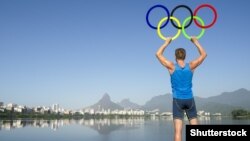 Спортсмен тримає олімпійські кільця на тлі блакитного неба перед Літніми Олімпійськими іграми 2016 року у Ріо-де-Жанейро
