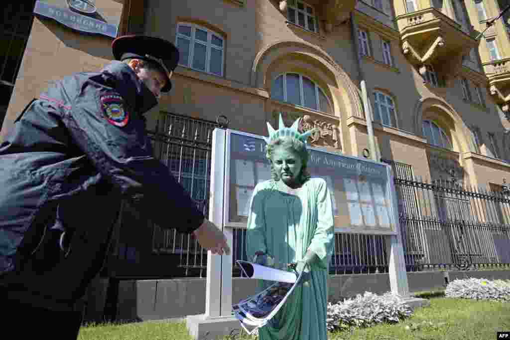 A woman passes photographs of riots in the United States to a Russian policeman while wearing a Statue of Liberty costume during a protest in front of the U.S. Embassy in Moscow. (AFP/Aleksandr Nemenov)