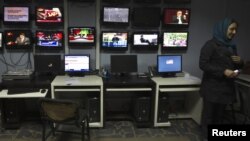 A news reporter stands next to TV screens at Tolo television in Kabul. Tolo's journalists have been arrested and received death threats because of critical reports about government corruption and vote fraud.