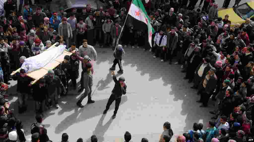 Syrian mourners, one carrying the pre-Ba'ath national flag adopted by the rebel movement, carry the body of a youth reportedly killed in violence in Idlib before his burial on February 23. (AFP PHOTO/BULENT KILIC)