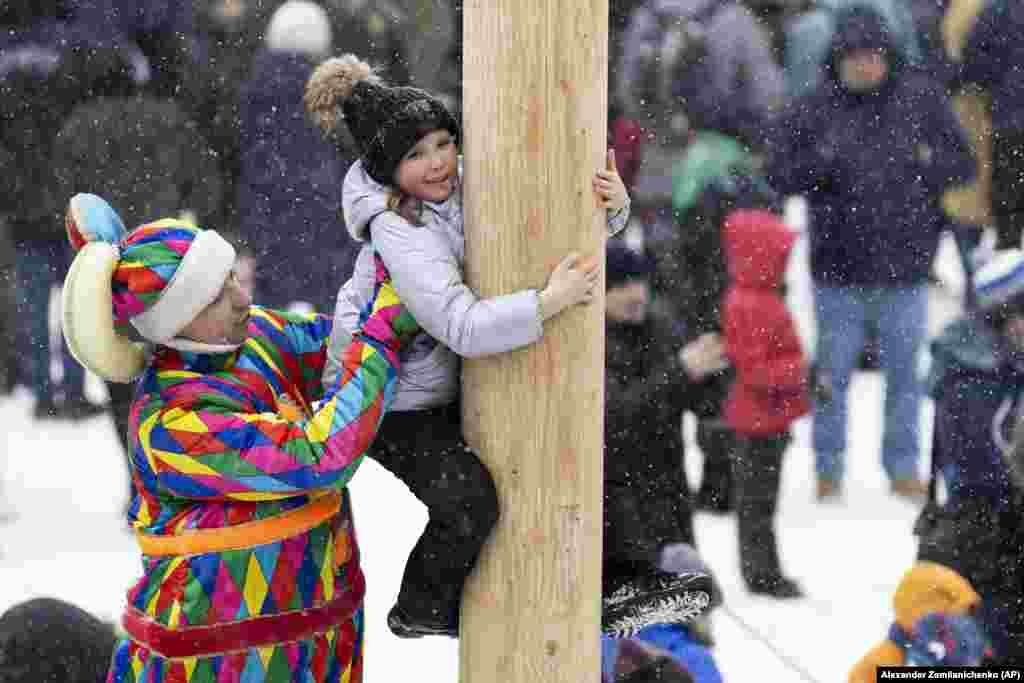 A Russian clown helps a girl to climb up a wooden pole to get a prize during Maslenitsa celebrations at the Izmailovsky Kremlin in Moscow.
