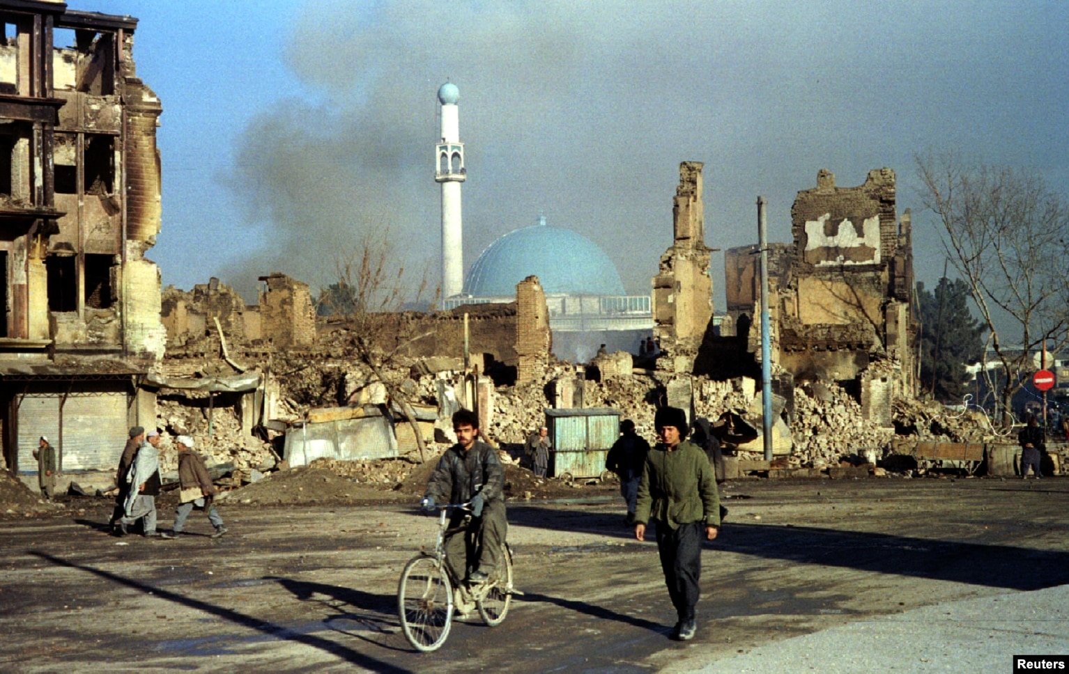 Një fotografi e vitit 1994 tregon afganët derisa kalojnë pranë ndërtesave të shkatërruar në Kabul nga lufta civile.