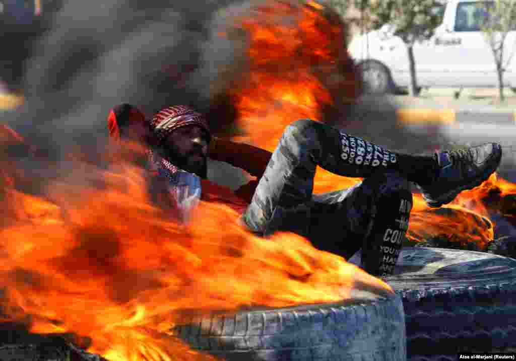 An Iraqi demonstrator sits amid burning tires blocking a road during ongoing anti-government protests in Najaf, Iraq. (Reuters/Alaa al-Marjani)