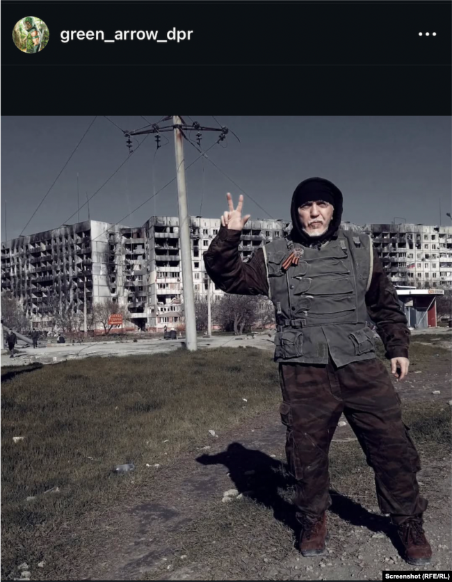 Zllatko Novkoviq fotografohet me tre gishta të ngritur para ndërtesave të shkatërruara nga sulmet ruse në qytetin Mauripol në Ukrainë. (Postim në Instagram nga viti 2022)