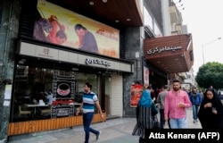 Iranians walk past a poster for the film Damascus Time by Iranian director Ebrahim Hatamikia in Tehran.