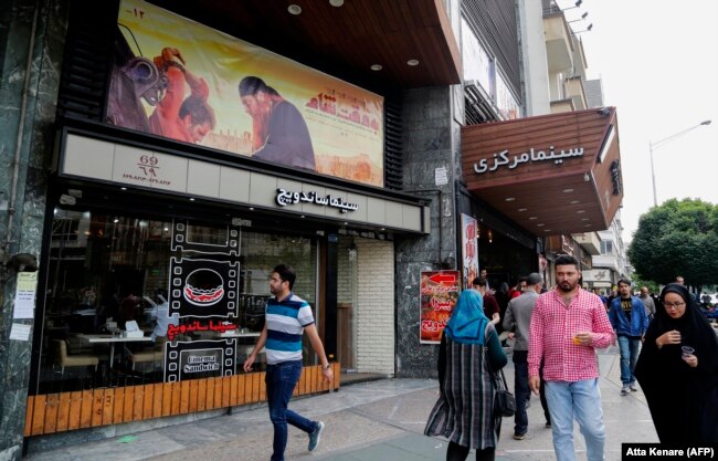 Iranians walk past a poster for the film Damascus Time by Iranian director Ebrahim Hatamikia in Tehran.