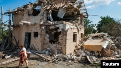 A local resident carries belongings from the ruins of her house, which was destroyed in a Russian missile strike in the Kyiv region on August 27.