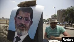 Бийликтен четтетилген президент Мохаммед Мурсинин тарапкери анын сүрөтүнүн жанында Куран окуп жатат. Раба ал-Адвийа жамы мечитинин аянты, Каир. 11.7.2013. (REUTERS/Amr Abdallah Dalsh).