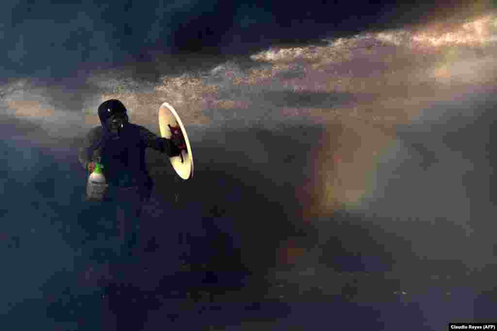 A Chilean protester protects himself from the spray of a police water cannon with a makeshift shield during a demonstration against the government in Santiago on November 26. (AFP/Claudio Reyes)