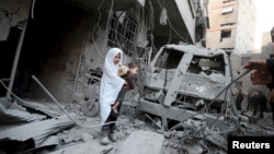 Сирийская девочка с ребенком на руках осматривает поврежденные здания, которые по словам активистов, пострадали от авиаударов ВВС России в сирийском городе Дума.