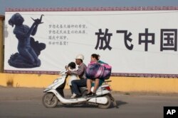 "Қытайды шарықтатайық" деген пропагандалық жазудың алдынан өтіп бара жатқан адамдар. Қашғар, Шыңжаң, 31 тамыз 2018 жыл.