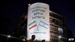 Israel -- People walk past a large billboard depicting both national flags of Israel (R) and Iran reading 'The Iranian embassy in Israel will open soon' in central Tel Aviv, August 27, 2015