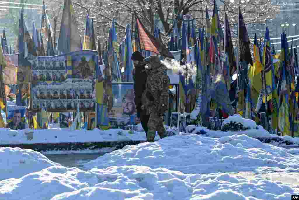 Un bărbat și un militar, trecând pe lângă memorialul în cinstea soldaților căzuți, improvizat în Piața Independenței din Kiev, 18 ianuarie.