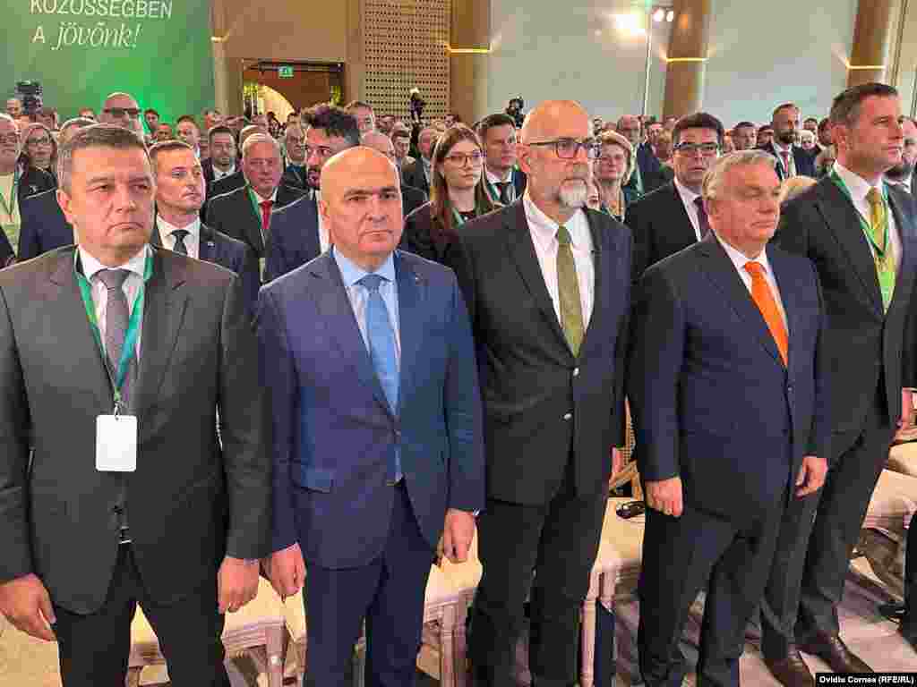Liderul PSD, Sorin Grindeanu (în stânga), premierul României, Ilie Bolojan, liderul UDMR, Kelemen Hunor, premierul maghiar Viktor Orbán și vicepremierul român Tánczos Barna, la intonarea imnului României, urmat de cel al Ungariei.