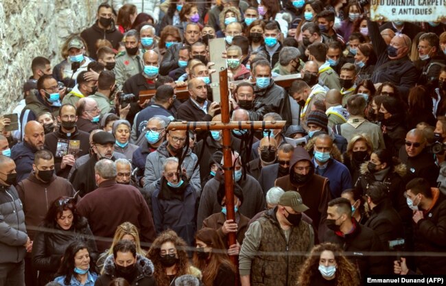 Христианские верующие несут деревянный крест вдоль Виа Долороза (Путь страданий) в Старом городе Иерусалима во время шествия Страстной пятницы, 2 апреля 2021 г.