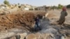 Men stand around a crater caused by what activists say was a Russian air strike in Latamineh on September 30 in the northern countryside of Hama.