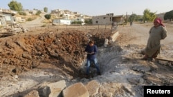 Men stand around a crater caused by what activists say was a Russian air strike in Latamineh on September 30 in the northern countryside of Hama.