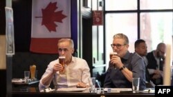 Britanski premijer Keir Starmer (desno) i kanadski premijer Mark Carney piju pivo u pubu Royal Oak u Ottawi, Kanada, 14. juna 2025. godine dok na televiziji gledaju finalnu hokejašku utakmicu Stanley Cupa, uoči samita lidera G7.