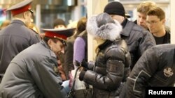 A police officer checks the hand baggage of a woman as people wait in a line to pass through a metal detector at Moscow's Domodedovo airport on January 25, less than 24 hours after the devastating bombing.