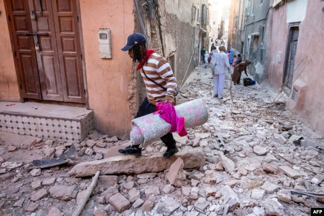Një burrë duke ecur me gjësendet e tij nëpër gërmadha në një rrugicë në qytetin e vjetër, Marakesh, pas tërmetit shkatërrues më 9 shtator 2023.