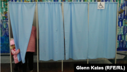 A little girl peeks around the curtain as a family member casts her ballot. 