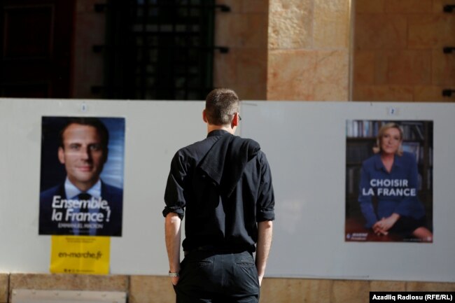 Një person shikon posterët e Macronit dhe Le Penit, që garuan në rundin e balotazhit në zgjedhjet e vitit 2017.