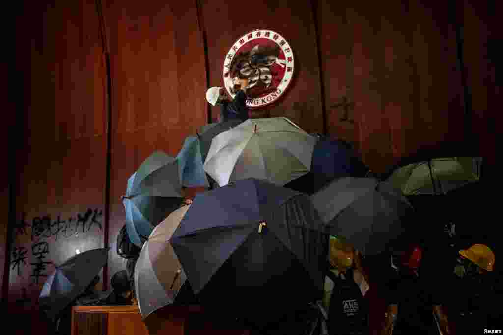 Демонстранттар Мыйзам чыгаруу кеңешинин имаратына чабуул жасагандан кийин, Гонконгдун эмблемасына боёк чачып жаткан киши. 1-июль, 2019-жыл.