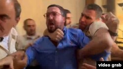 სასამართლოში გადაღებულ კადრებში ჩანს რომ მას მანდატურები აკავებენ და შეჰყავთ ერთ-ერთ ოთახში.