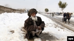 An Afghan man sits on a snow-covered road after heavy snowfall on the outskirst of Kabul