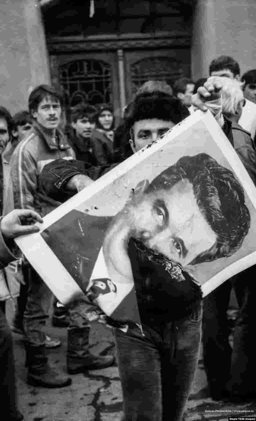 Un bărbat flutură un portret parțial ars cu Ceaușescu, în Târgu Mureș, pe 22 decembrie 1989, în timpul revoluției care i-a scăpat pe români de disprețuitul dictator.&nbsp; &nbsp;