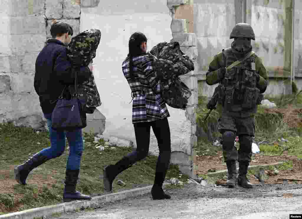 Two women, believed to be Ukrainian servicewomen, carry their uniforms as they walk past an armed man, believed to be a Russian serviceman, while leaving a military base in Perevalnoye, near Simferopol in Crimea on March 19. (Reuters/Shamil Zhumatov)