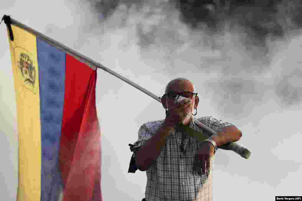 An anti-government protester carrying a Venezuelan flag covers his face amid tear gas fired by soldiers loyal to President Maduro during an attempted military uprising in Caracas on April 30. (AP/Boris Vergara)